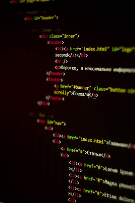Close-up of a computer monitor displaying colorful HTML and JavaScript code, set on a desk in a well-lit office environment. The screen shows lines of code in red, blue, green, and white text on a dar